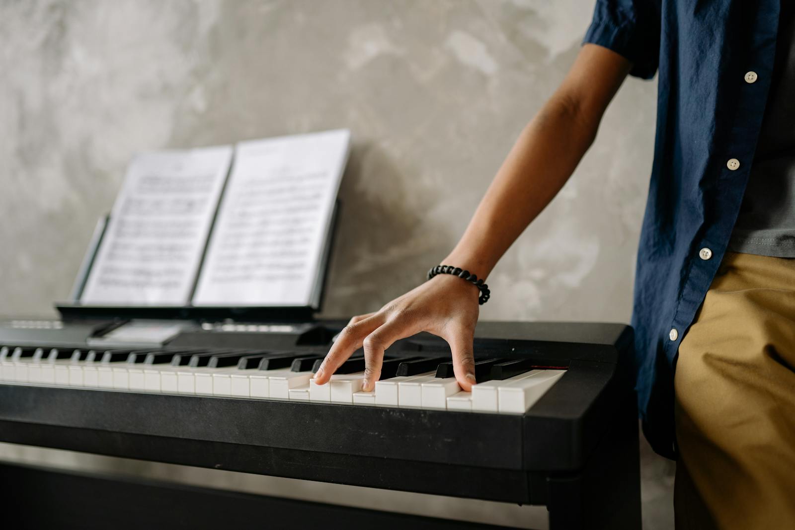 Close-up of a child playing a keyboard indoors with sheet music visible.